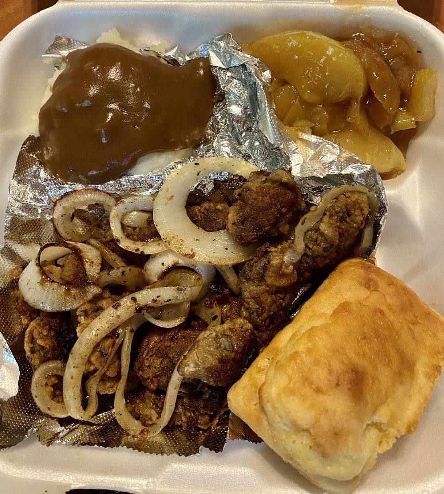 A takeout dinner plate with onions, gravy, fried apples and a biscuit